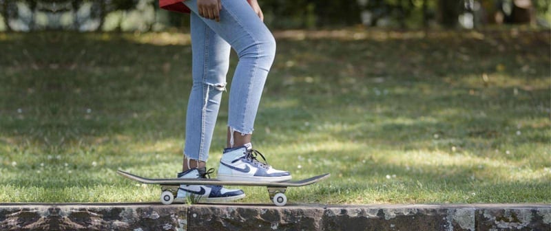 Beine in Jeans und Sneakern auf einem Skateboard vor einer Wiese